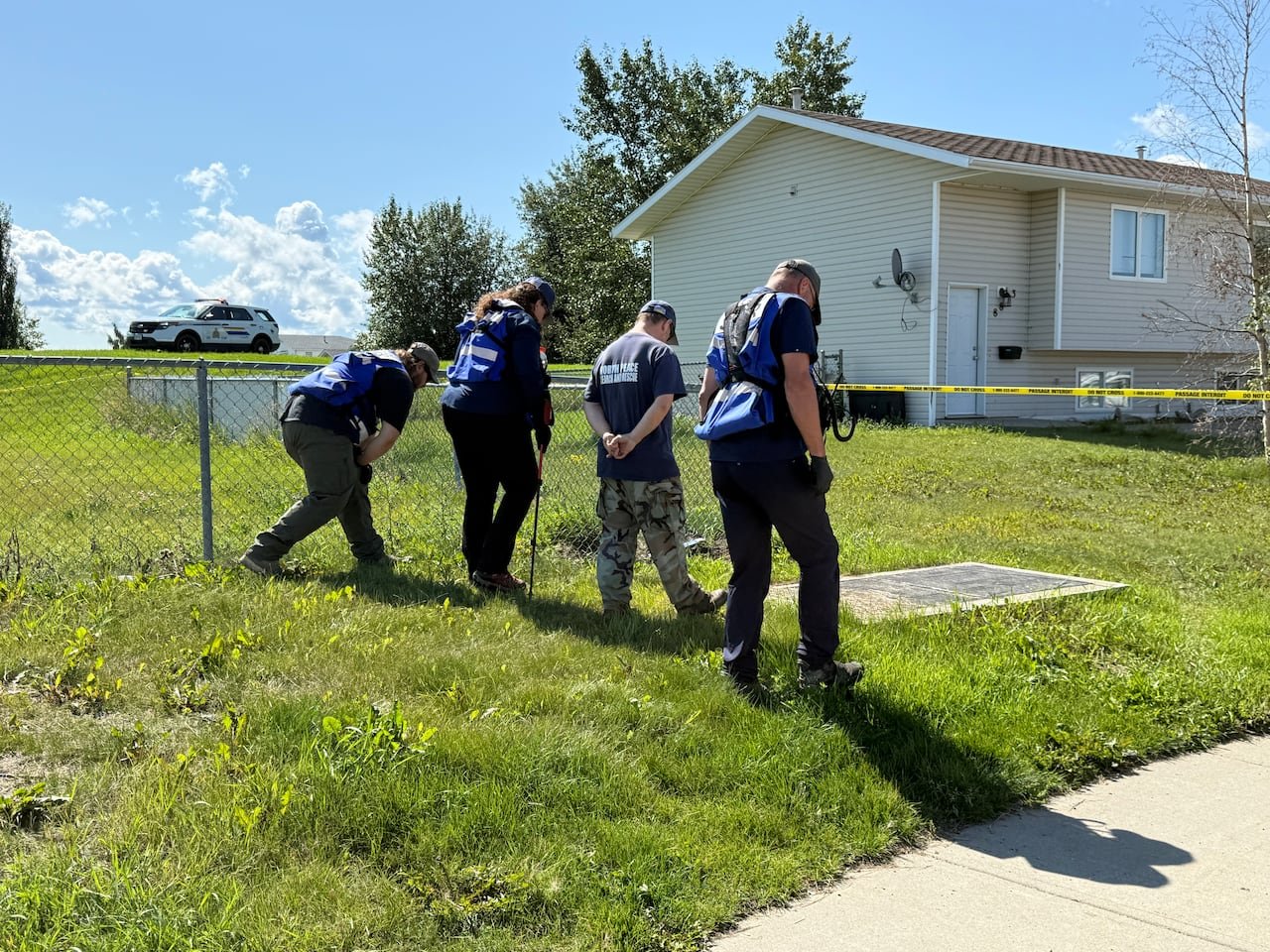 default-273 four uniformed investigators walking towards a house cordoned off with yellow police tape across a grassy yard