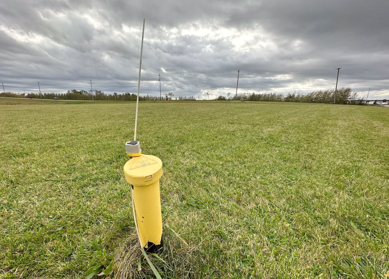 default-57 A yellow metal pipe with a metal cap on it and a metal pole sticking out the top is seen in the middle of a field of green grass.